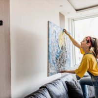 young woman hanging art picture on wall and decorating living room - home decoration stock pictures, royalty-free photos & images