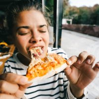 young woman is eating cheese pizza with pleasure - junk food stock pictures, royalty-free photos & images