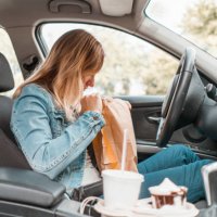 young woman opening take out food bag in a car - junk food stock pictures, royalty-free photos & images