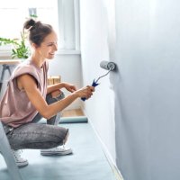 young woman painting wall with paint roller while crouching at home - home decoration stock pictures, royalty-free photos & images