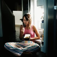 young woman sitting by open refrigerator, eating ice cream - junk food stock pictures, royalty-free photos & images
