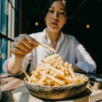young woman sitting by the window in restaurant enjoying french fries and meal - junk food stock pictures, royalty-free photos & images