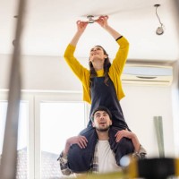 young woman sitting on boyfriend shoulders installing light bulb in new home - home decoration stock pictures, royalty-free photos & images