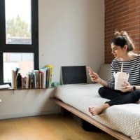 young woman sitting on couch at home having asian takeaway food and using cell phone - junk food stock pictures, royalty-free photos & images