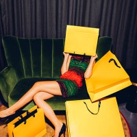young woman sitting on couch hiding her face behind a shopping bag - fashion stock pictures, royalty-free photos & images