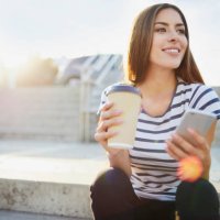 young woman sitting on stairs in the city with phone and coffee - junk food stock pictures, royalty-free photos & images