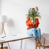 young woman sitting on table holding flower vase in front of her face - home decoration stock pictures, royalty-free photos & images