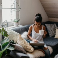 young woman sitting on the couch with cup of coffee using laptop - home decoration fotografías e imágenes de stock