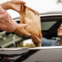 young woman smiling at service person at the drive through while receiving her takeaway order - junk food stock pictures, royalty-free photos & images