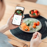 young woman using calorie counter app on smartphone while eating salad - food stock pictures, royalty-free photos & images