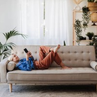 young woman using mobile phone lying on sofa at home - home decoration stock pictures, royalty-free photos & images