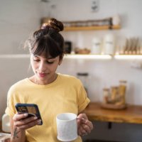 young woman using the mobile phone while drinking coffee or tea at home - coffee stock pictures, royalty-free photos & images