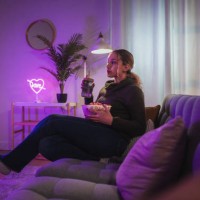 young woman watching tv and eating popcorn in cozy living room with neon lights - home decoration stock pictures, royalty-free photos & images