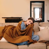 young woman wearing pajamas and a blanket sitting on sofa - home decoration stock pictures, royalty-free photos & images