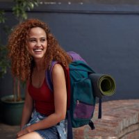 young woman with backpack smiling, while sitting in courtyard - travel stockfoto's en -beelden