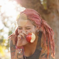 young woman with pink dreadlocks giggling whilst eating apple in park - food stock pictures, royalty-free photos & images