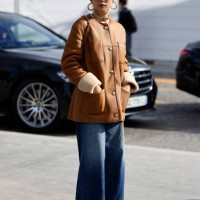 Yoyo Cao wears brown jacket, brown Chanel bag with fur detail, black checked hat, blue jeans, brown boots, outside Chanel, during Womenswear...