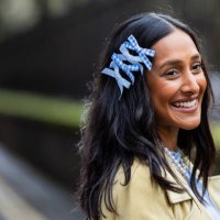Zeena Shah wears blue bows in hair, blue dress, pearl necklace, beige coat, blue bag outside Eudon Choi during London Fashion Week February 2024 on...