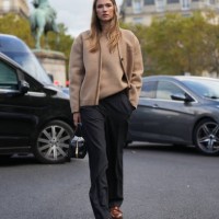 Zita D'Hauteville wears a pale / pastel brown / beige Miu Miu wool cardigan, a pullover, black pants, a black leather bag, brown leather shoes ,...