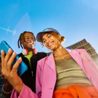 zwei freunde der generation z, die gemeinsam ein smartphone benutzen. aufnahme aus dem tiefwinkel mit modernen gebäuden im hintergrund. social media und freundschaftskonzept. - fashion stock-fotos und bilder