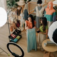 zwei junge asiatinnen präsentieren dem publikum ein kleidungsstück, während sie live für ihren online-shop verkaufen. - fashion stock-fotos und bilder