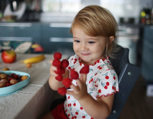 a baby girl playing with raspberries on her fingers, in the kitchen - food stock pictures, royalty-free photos & images