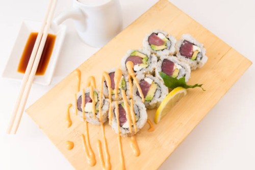 a bamboo cutting board sits with a sushi maki roll made with tuna, avocado and cream cheese - junk food stock pictures, royalty-free photos & images