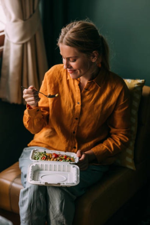 a beautiful blonde female sitting in her living room eating some healthy food - junk food stock pictures, royalty-free photos & images