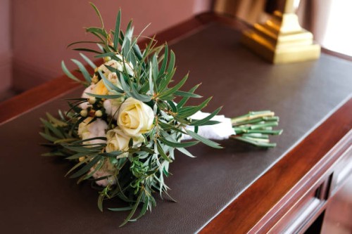 a beautiful wedding bouquet lies on the table, chest of drawers or bedside table, close-up. bouquet of different flowers and green leaves, tied with a satin ribbon, blurred background. wedding theme. a beautiful combination o