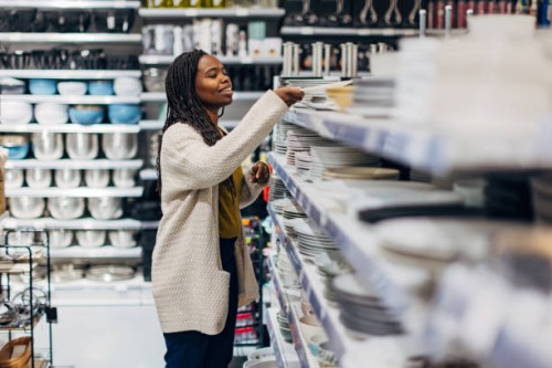 a black woman stands next to a shelf of plates displayed in a department store. she chooses dishes for her new apartment - home decoration stock pictures, royalty-free photos & images