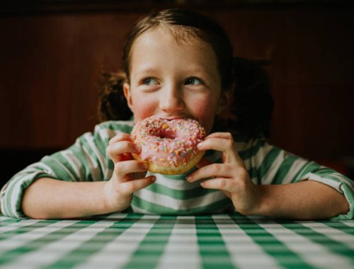 a child smiles as she takes a bite of a pink glazed donut with sprinkles - junk food stock pictures, royalty-free photos & images