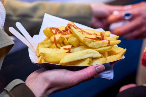 a close-up of a hand holding tasty takeaway chips at night with ketchup - junk food stock pictures, royalty-free photos & images