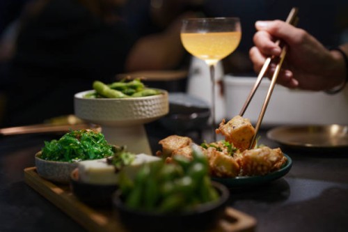 a close-up view of a woman's hand reaching for a plate of vegan deep-fried tofu in a cozy vegetarian restaurant. - food stock pictures, royalty-free photos & images