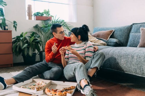 a couple enjoying eating pizza while sitting on the floor of their cozy living room - food stock pictures, royalty-free photos & images