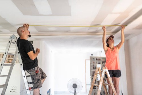 a couple undergoing renovations measure the distances to place the spotlights on the ceiling during an electrical renovation... - home decoration stock pictures, royalty-free photos & images