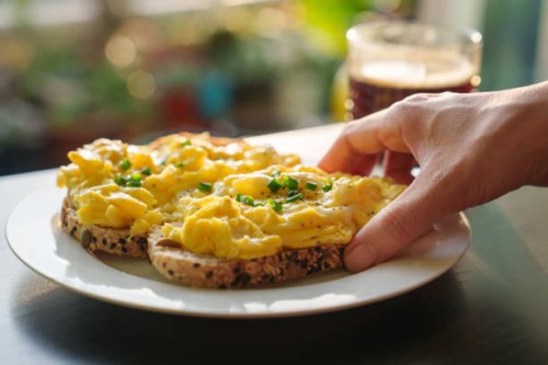 a cropped image of a woman's hand holding a piece of toasted bread with scrambled eggs on top, as she enjoys a healthy breakfast in the morning - food stock pictures, royalty-free photos & images