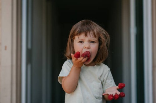 a cute toddler girl with funny facial expression eating raspberry - food stock pictures, royalty-free photos & images