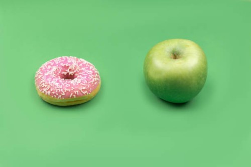 a donut and an apple on green background. - junk food stock pictures, royalty-free photos & images