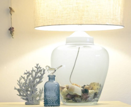 a glass lamp filled with shell illuminates some object at a beach house sideboard. - home decoration stock pictures, royalty-free photos & images