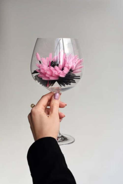 a glass with disposable eyebrow and eyelash brushes in the hands of the girl. disposable eyebrow and eyelash brushes. pink and black brushes. woman's hand. gray universal background. - nails art stock pictures, royalty-free p