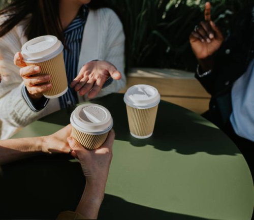 a group of colleagues sit at a table outdoors and enjoy some takeaway coffees - coffee stockfoto's en -beelden
