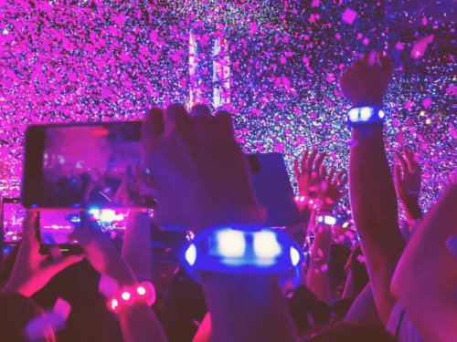a group of people ecstatic with led bracelet recording with smartphone the concert with hands up, confetti and energy. - concert stock pictures, royalty-free photos & images