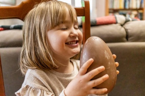 a happy little girl with her eyes closed holding a chocolate easter egg at home - junk food stock pictures, royalty-free photos & images