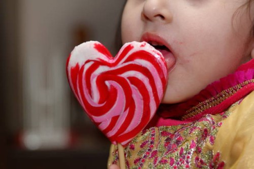 a little cute girl eating and licking heart shape lollipop. - junk food stock pictures, royalty-free photos & images
