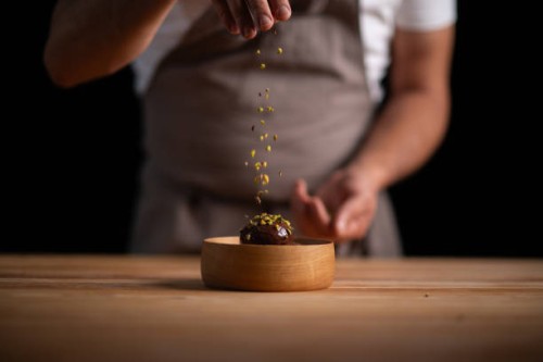 a male pastry chef pouring pistachios on profiteroles - food stock pictures, royalty-free photos & images