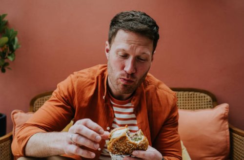 a man chews a large bite of a burger - junk food stock pictures, royalty-free photos & images