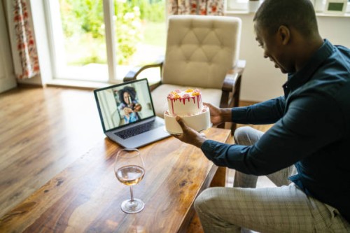 a man is showing his birthday cake to a friend via a video call on his laptop - junk food stock pictures, royalty-free photos & images