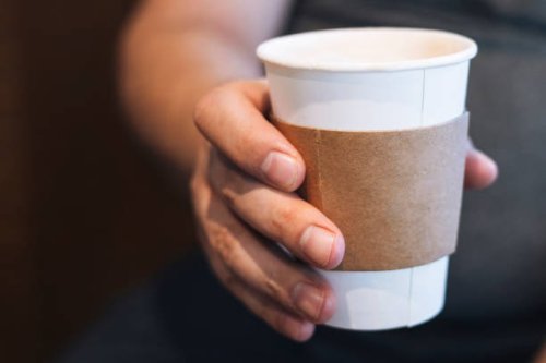 a person holding a takeaway coffee cup in hand with a cardboard sleeve, captured in a cozy indoor setting during the morning - junk food stock pictures, royalty-free photos & images