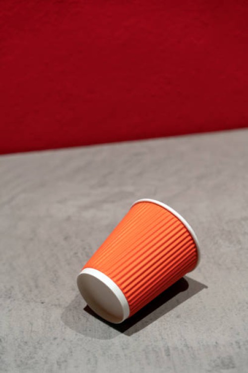 a red corrugated disposable paper coffee cup lying on a gray concrete table against a painted wall. takeaway, coffee to go. the concept of environmental pollution, recycling, recycling - junk food stock pictures, royalty-free