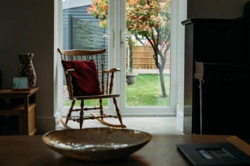 a rocking chair with a red velvet pillow by a large window and view of a beautiful garden - garden decoration stock pictures, royalty-free photos & images